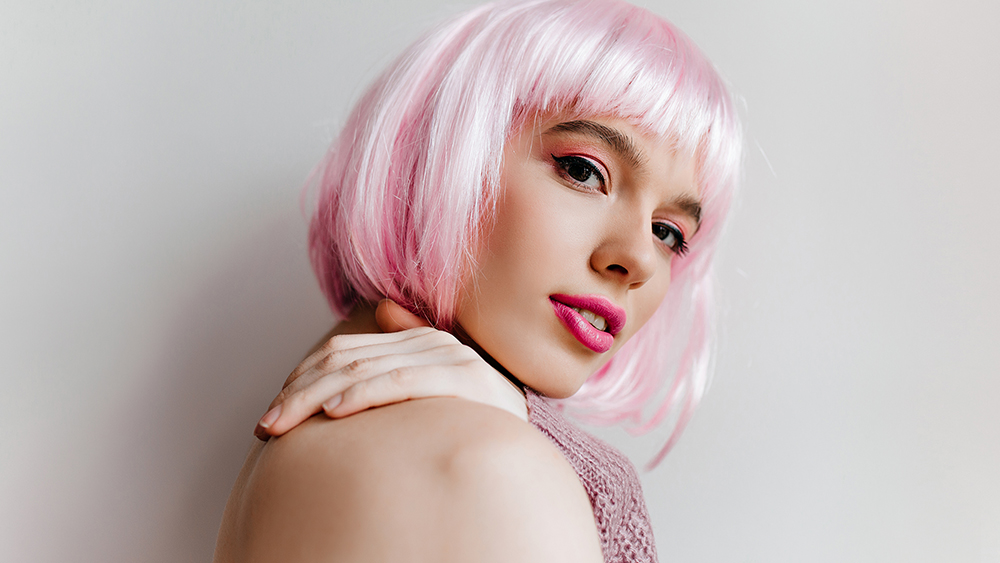 Dreamy young woman with bright makeup posing with pleasure in studio. Close-up photo of gorgeous female model in pink periwig looking to camera with smile.