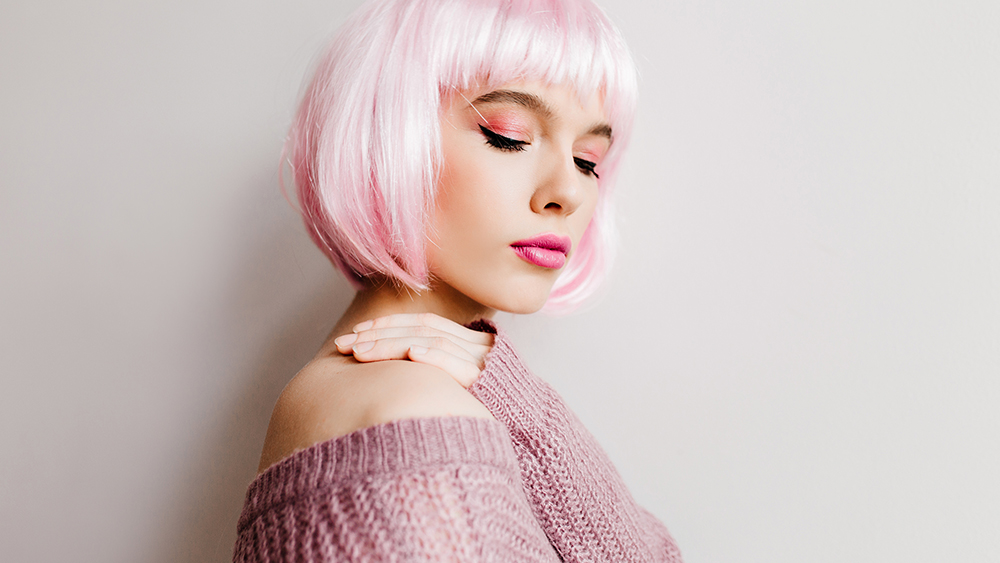 Spectacular young lady in stylish periwig standing with eyes closed. Pretty white girl wears pink wig posing in soft purple sweater.